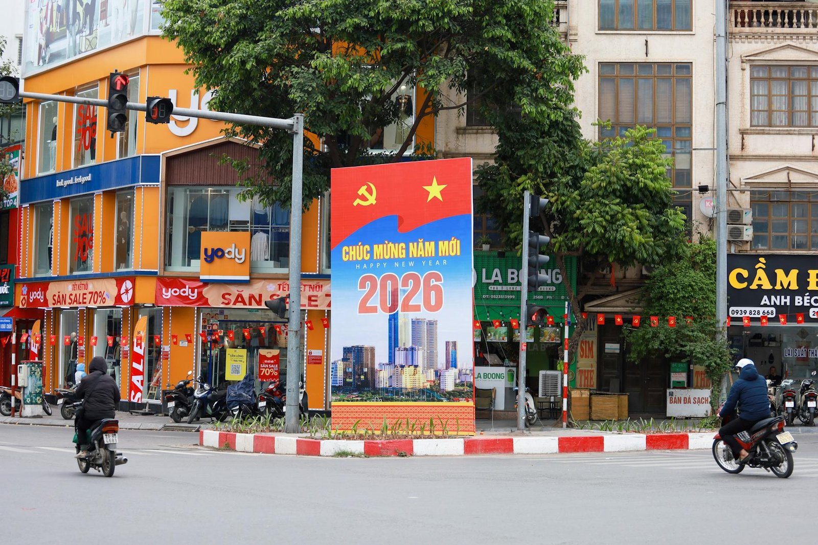 Vibrant Hà Nội street scene featuring a New Year 2026 billboard, motorcycles, and colorful shops.