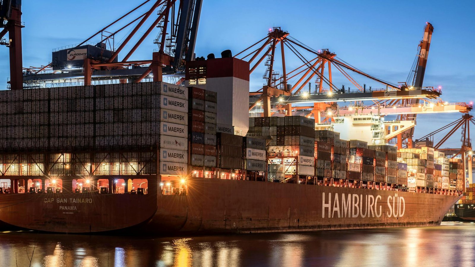 Large cargo ship docked in Hamburg port, showcasing busy industrial activity during twilight.