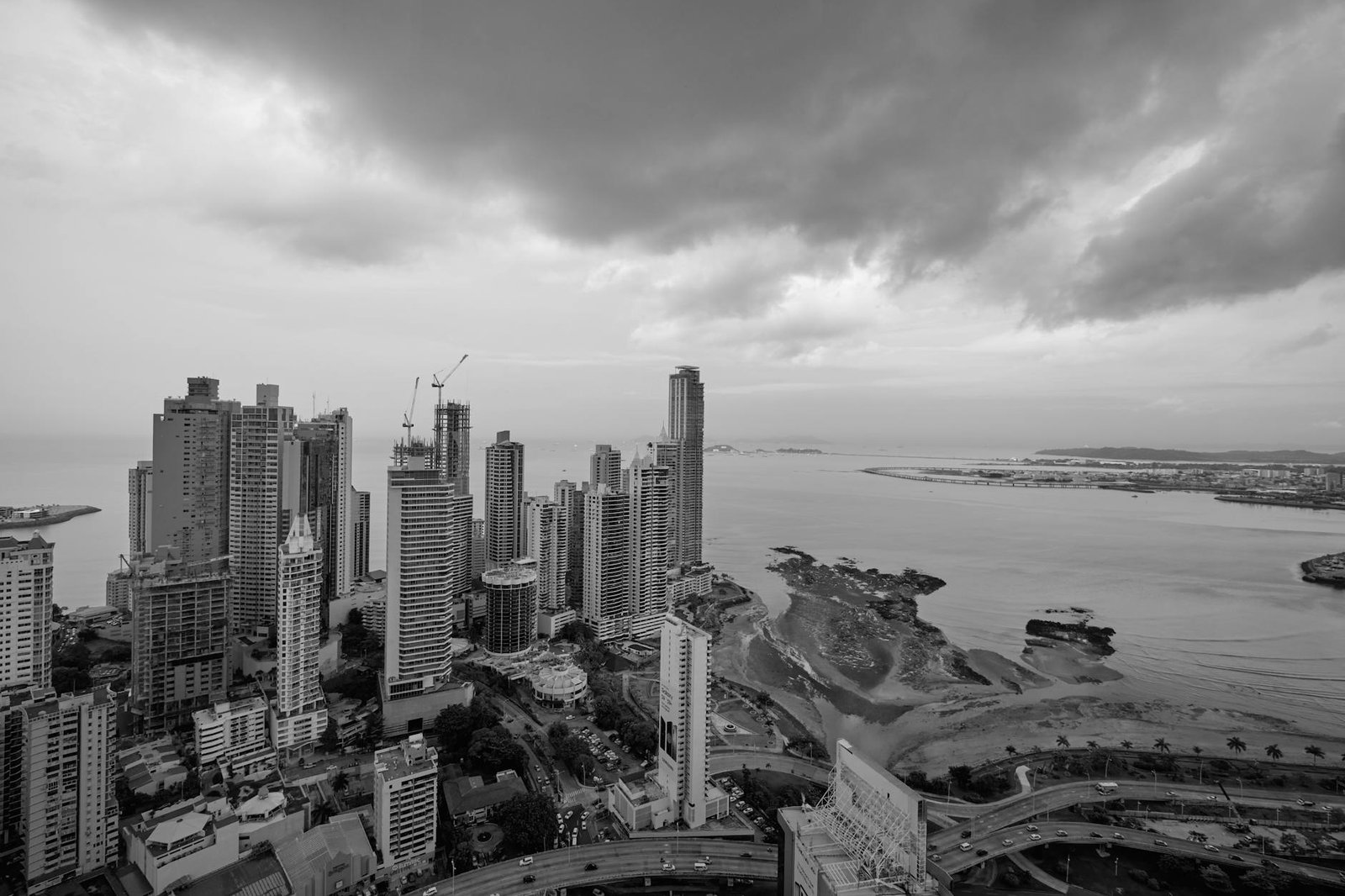 Black and white cityscape of contemporary skyscrapers located in downtown of coastal city under cloudy sky